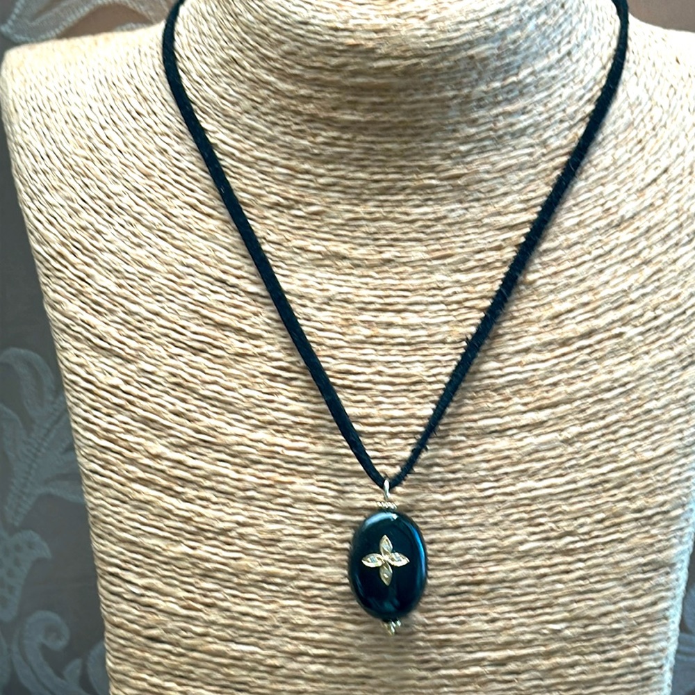 Black oval pendant with goldtone flower center suspended on black silk cord